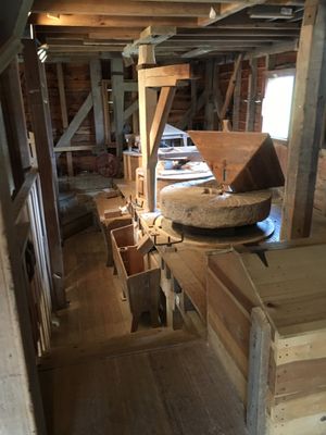 Color photo of interior of old gristmill building with large round mill stones and related equipment.